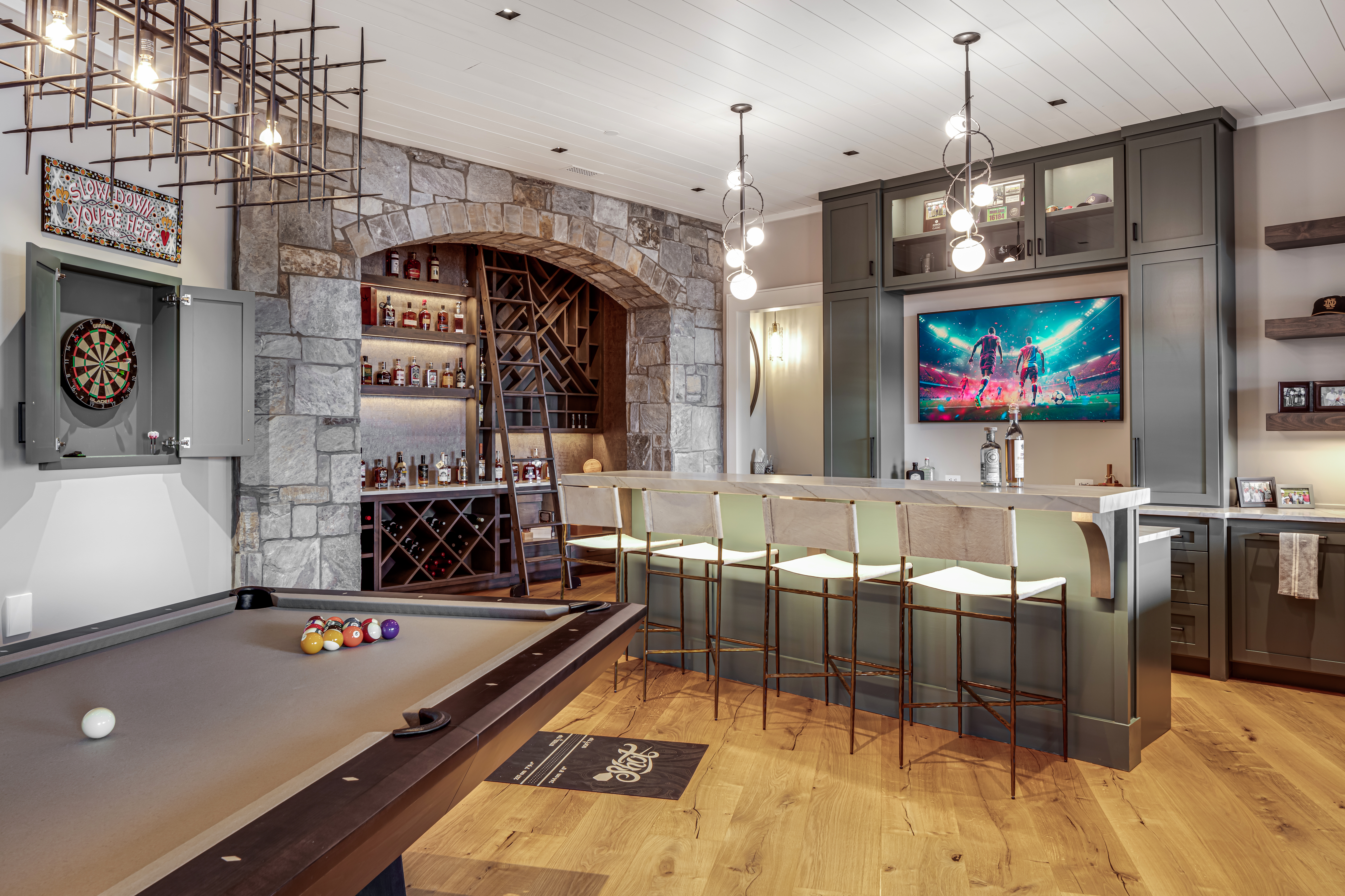 Custom basement bar and entertainment room with stone wine cellar arch and pool table — Mac & Morgan Interiors